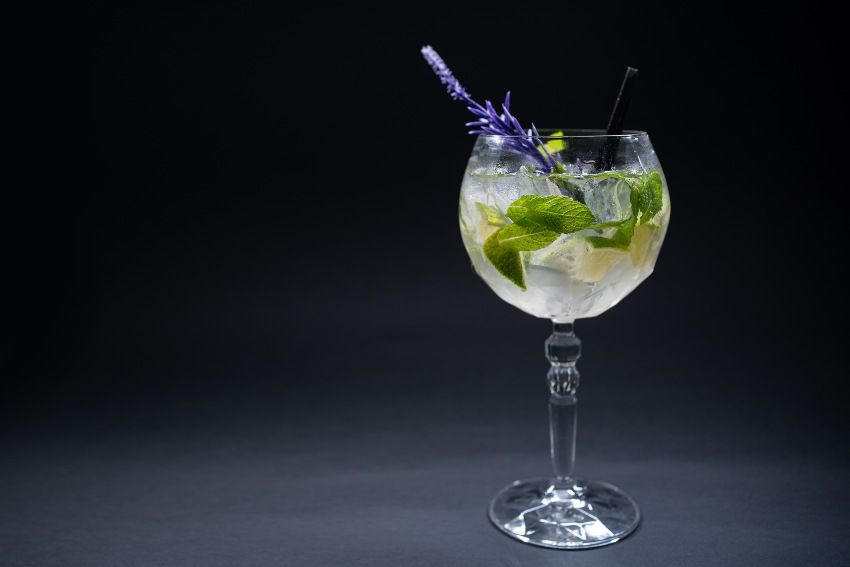 Sommerkaltes Hugo-Cocktailgetränk im Kelch mit Strohhalm auf dunklem Hintergrund