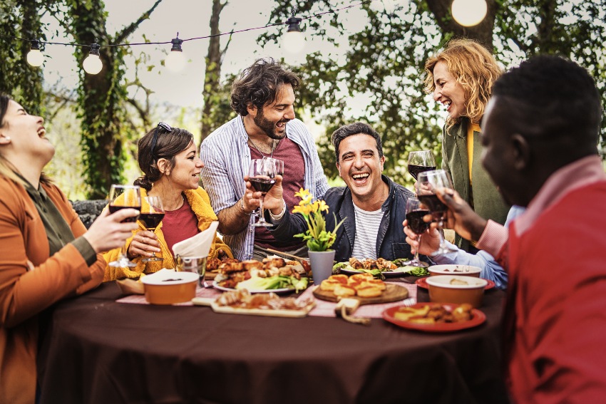 Gesellschaft von fröhlichen Menschen, die am Grilltisch plaudern und sich zusammen entspannen, gegrilltes Essen essen und Wein trinken - Zeitvertreib der besten Freunde beim Bauernbankett - Lifestyle-Konzept für multiethnische Menschen - Wein zum Grillen