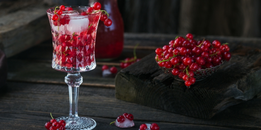 Sommergetränk mit weißem Sekt. Hausgemachter erfrischender Fruchtcocktail oder Punsch mit Champagner, roten Johannisbeeren, Eiswürfeln und Minzblättern auf dunklem Holzhintergrund.